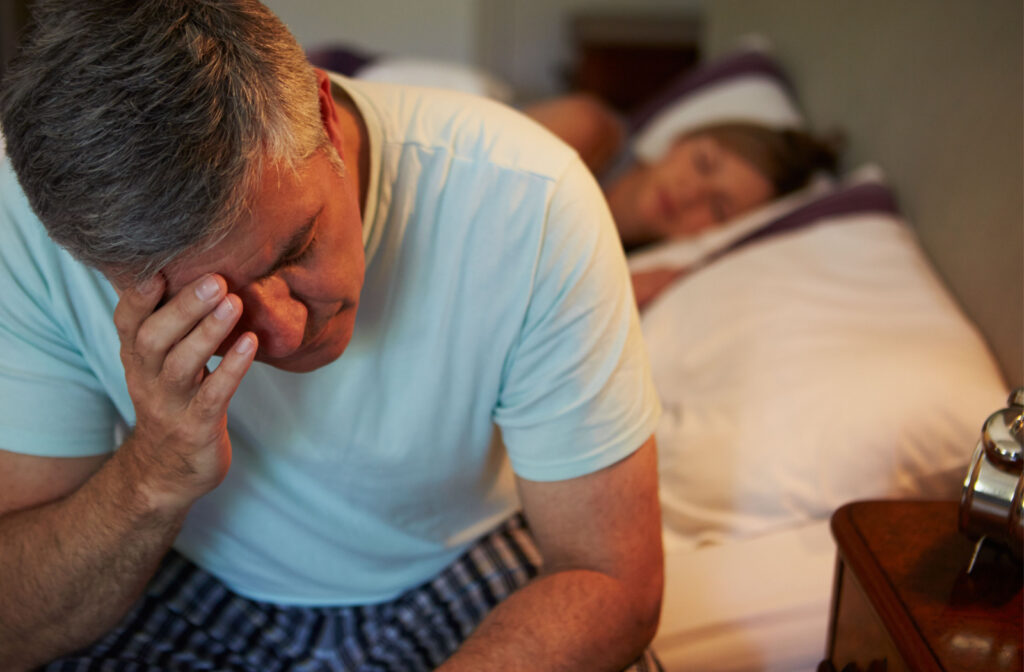 An adult man sitting on the edge of his bed, frustrated from not sleeping well due to sleep apnea
