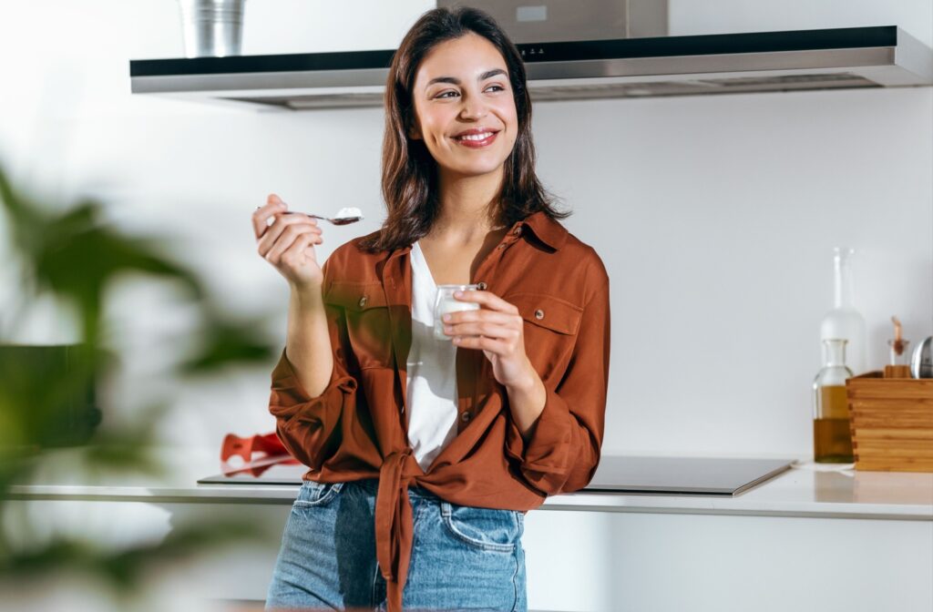 A young woman displays her beautiful clean smile while eating a yogurt, after her dental cleaning.