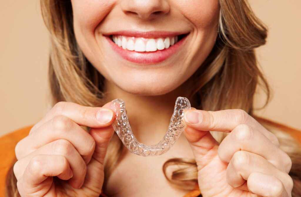 A closeup of a young woman's beautiful smile as she holds up her clear aligners.