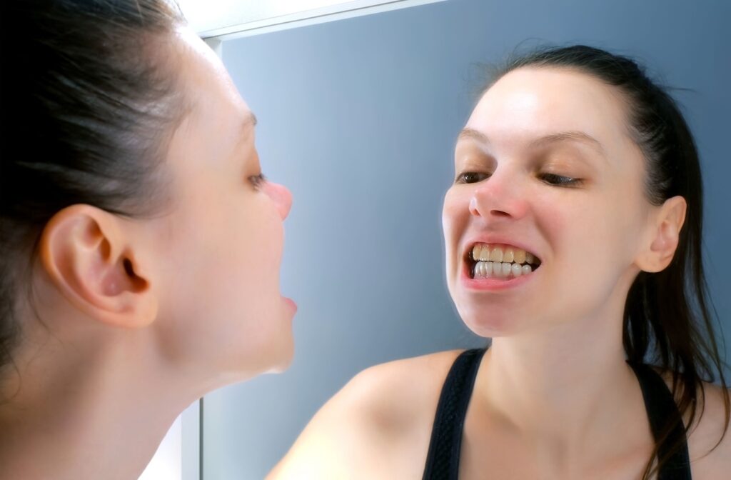 Woman examining her yellow teeth in the mirror.