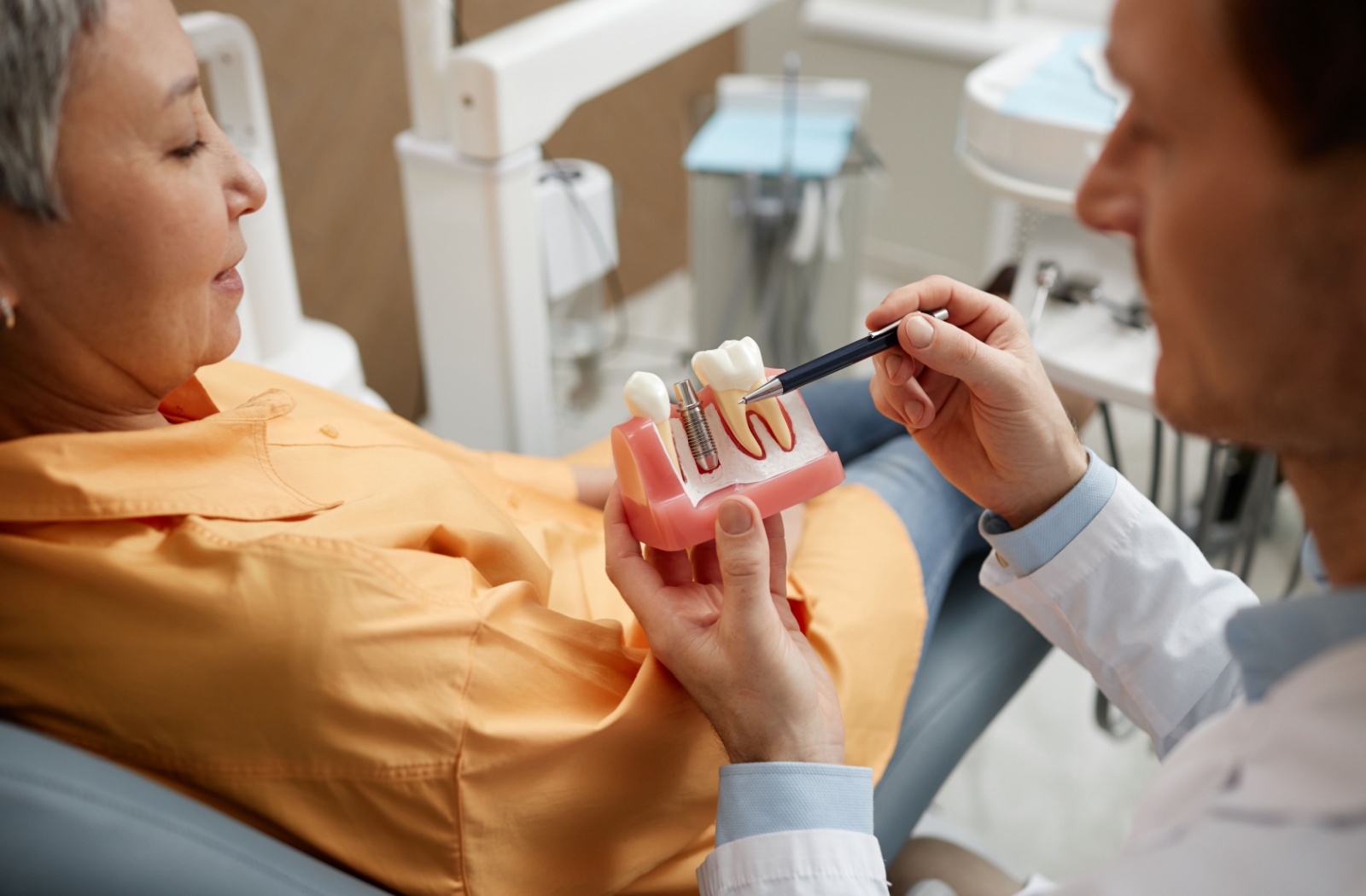 Closeup of male dentist holding and showing dental implant model to female patient.