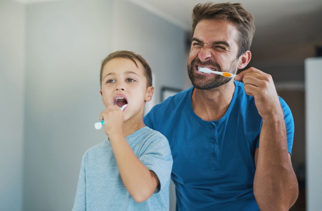 A person and their child enthusiastically brushing their teeth together in a bright bathroom promoting good oral hygiene