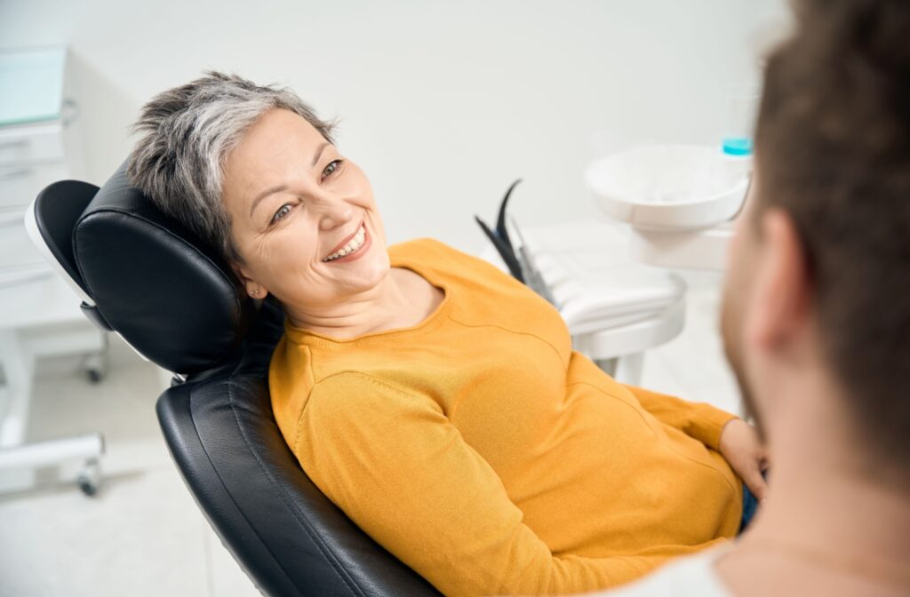 A smiling patient lying back in a chair while discussing symptoms with their dentist during a dental check-up.