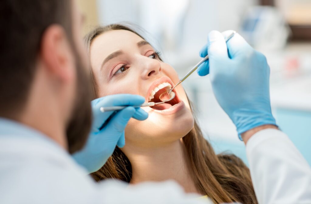 A dentist examines a patient's teeth with dental tools during a routine cleaning appointment.