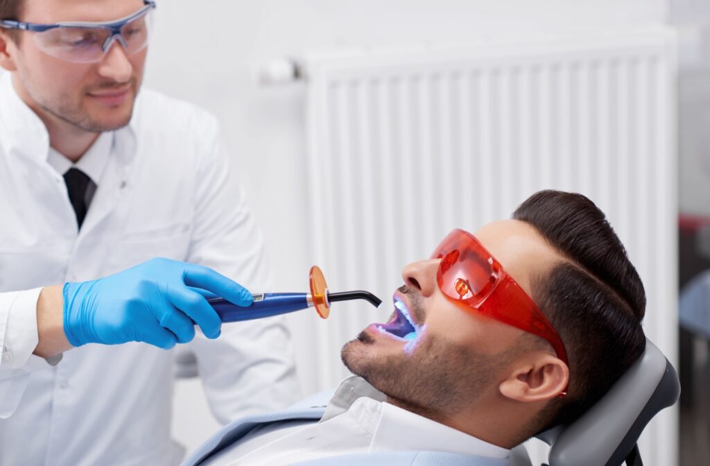 Male patient wearing protective glasses while a dentist uses a curing light to harden a tooth filling.