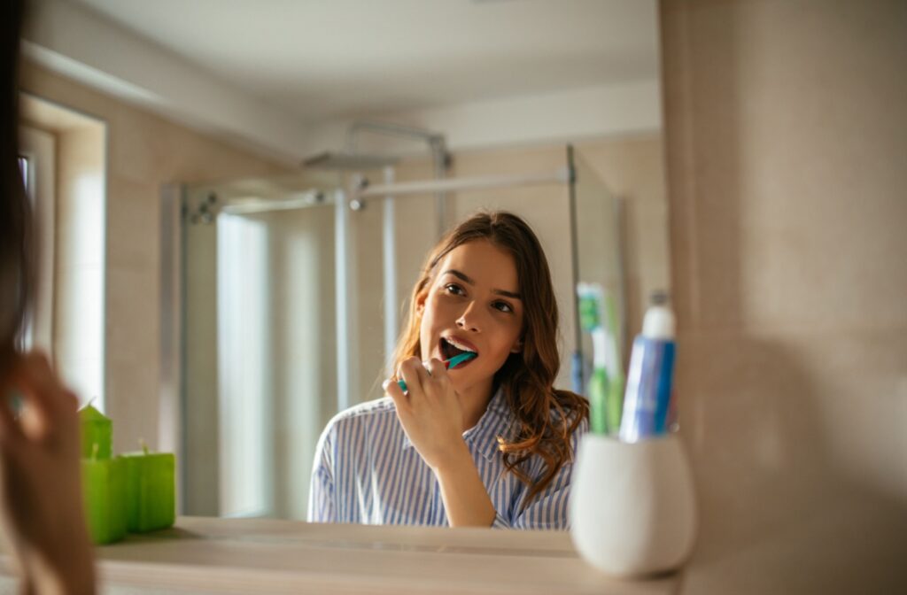 Person brushing their teeth in front of a bathroom mirror.
