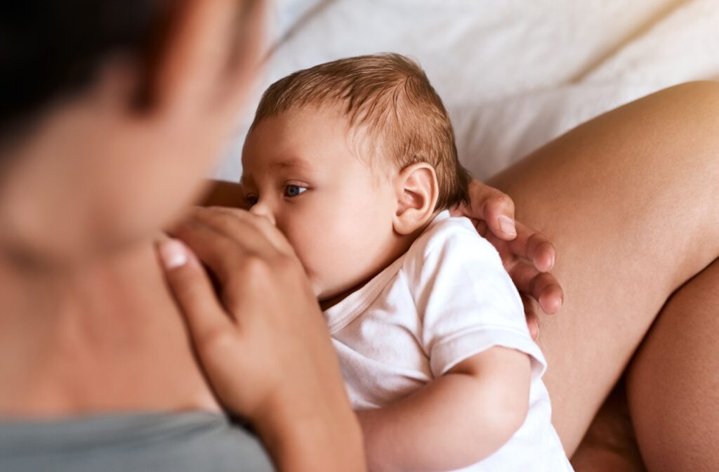 Over-the-shoulder view of a parent nursing a baby, with the parent's hand on their breast.