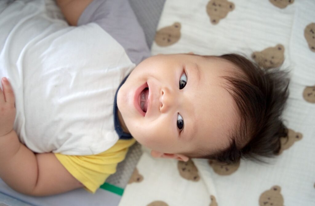 Overhead view of a smiling baby lying down, with visible frenulum between tongue and mouth.